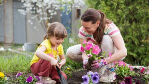 mother and child daughter plant flowers in the garden near the houme on spring day. Kid help mom work in the garden. slow life. enjoy the little things.