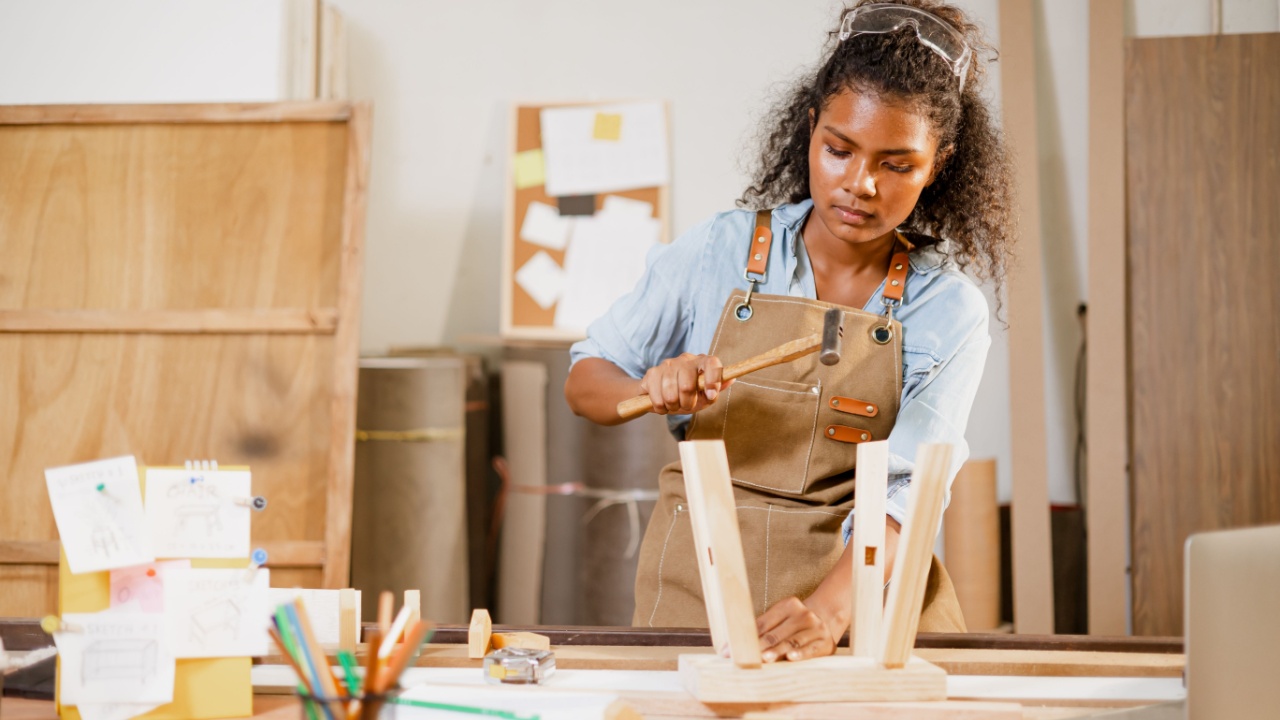 African black woman carpenter joiner working build wooden chair handcraft furniture in wood studio workshop.