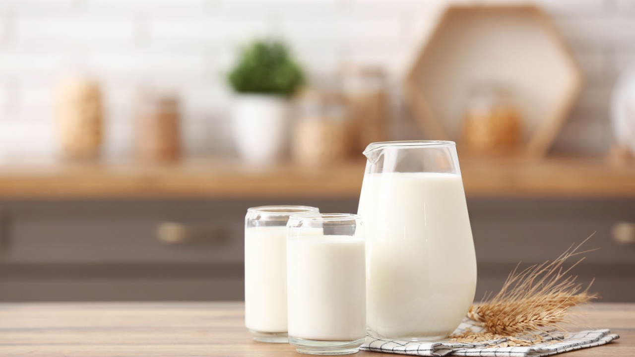 Glasses and jug of fresh milk with wheat ears on wooden table in kitchen