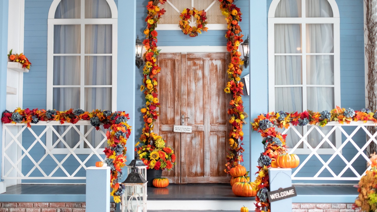 Entrance of house door decorated with autumn leaves for holiday. Fall yellow garland with leaves and pumpkins on door, fall decor. Halloween design home. Street lanterns on Entrance home