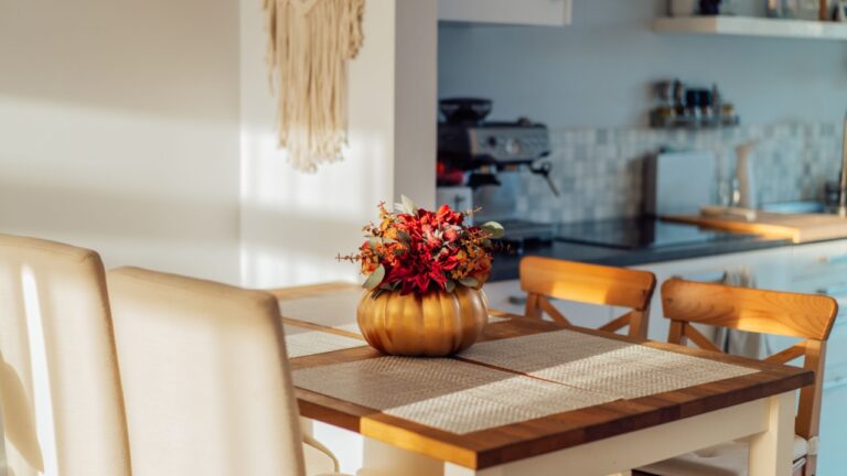 Autumn bouquet of bright artificial flowers in a golden pumpkin vase on a kitchen table counter with white modern kitchen background. Autumn home decor for Thanksgiving and Halloween holiday.
