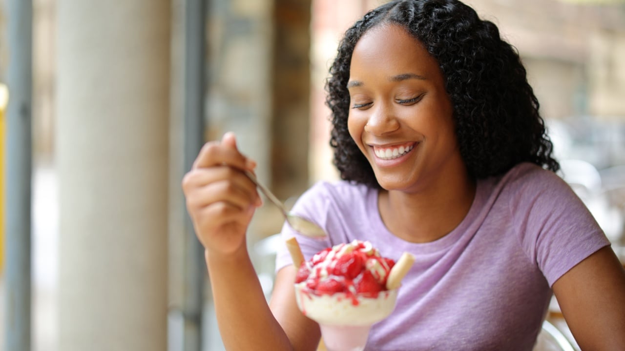Happy black woman eating ice cream in a restaurant terrace