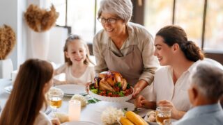 Thanksgiving Day, Autumn feast. Happy family sitting at the table and celebrating holiday. Grandparents, mother and children. Traditional dinner.