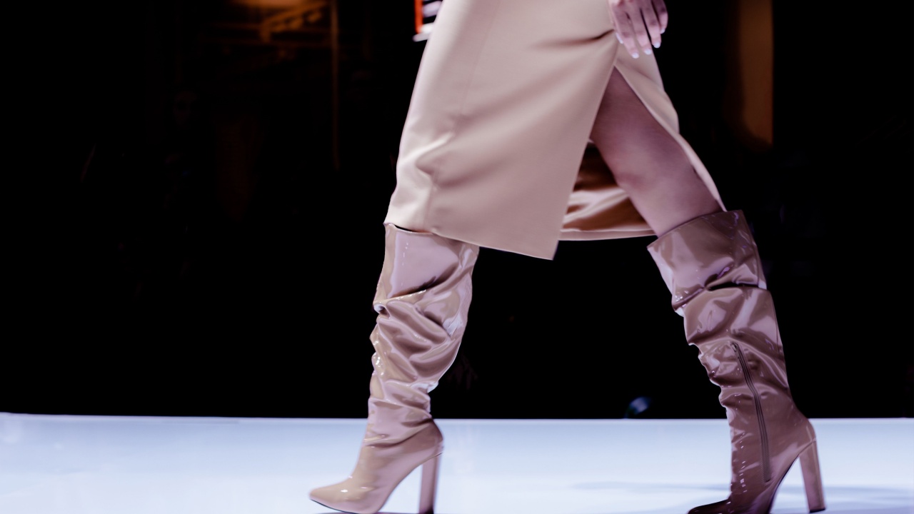 Fashion details of a beige skirt and patent leather high heel boots. Women's fashion and stylish accessories. Runway fashion show