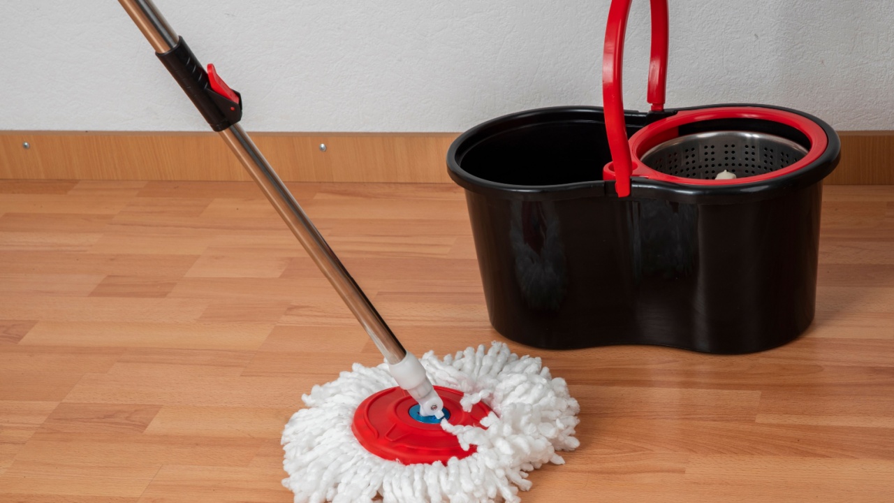 Cleaning concept mop and bucket. Cleaning products and spin mop with red details on the floor in an interior with a wooden floor or parquet, laminate