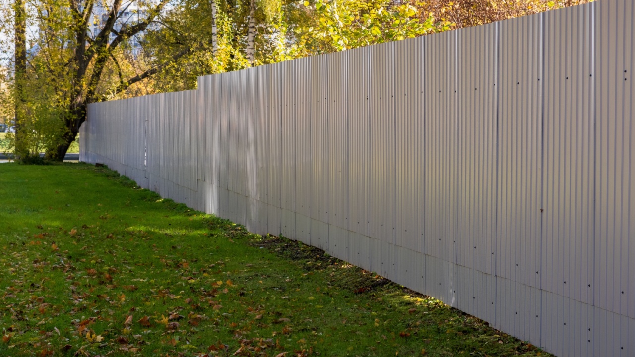 Metal fence made of corrugated sheets in an autumn park. The lawn area is fenced with a high fence.