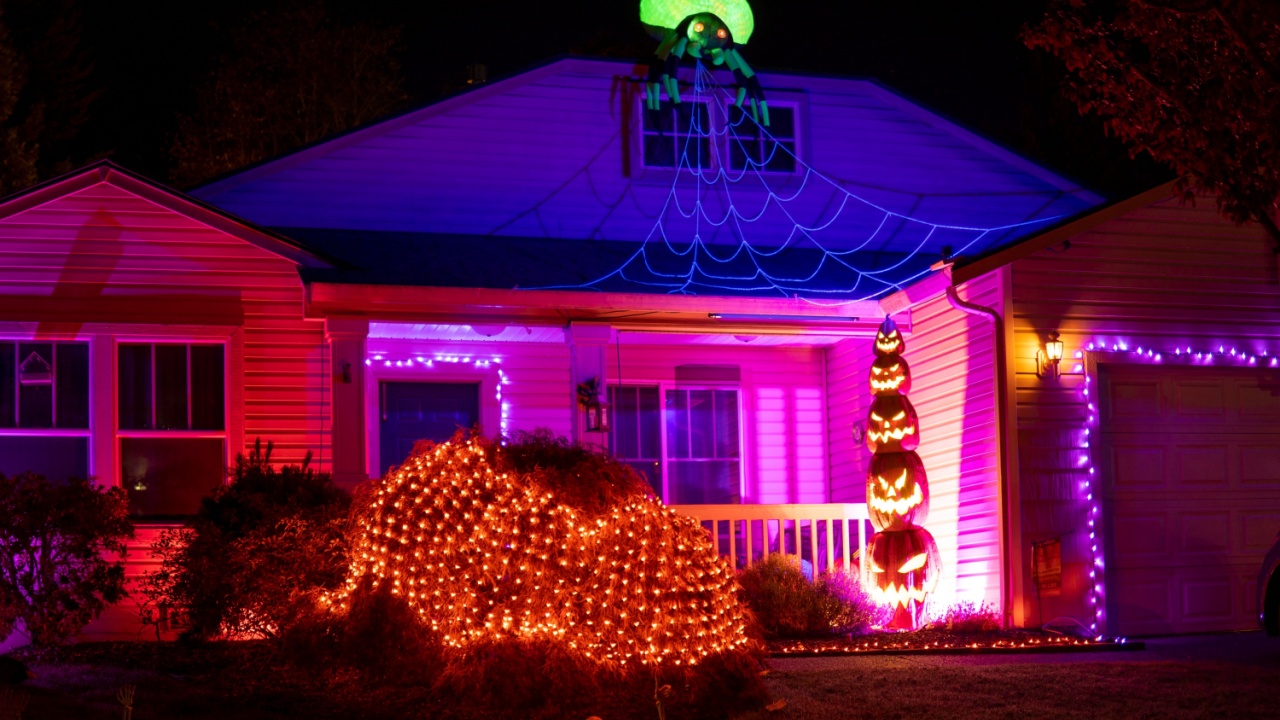 Beautiful Halloween decorations outside the house at night. House decorated with pink and orange lights, glow garlands, pyramid of pumpkins and green spider on the roof