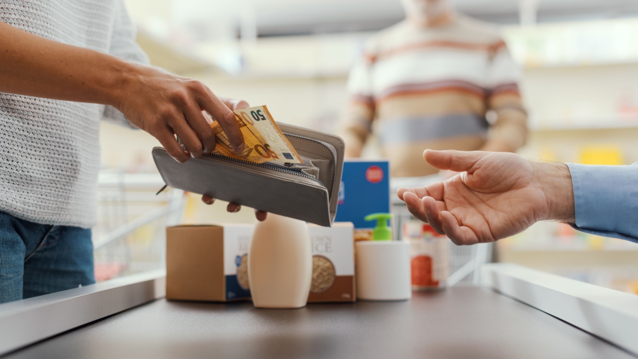 Cash payment at the supermarket: woman buying groceries and giving cash money to the cashier, hands close up