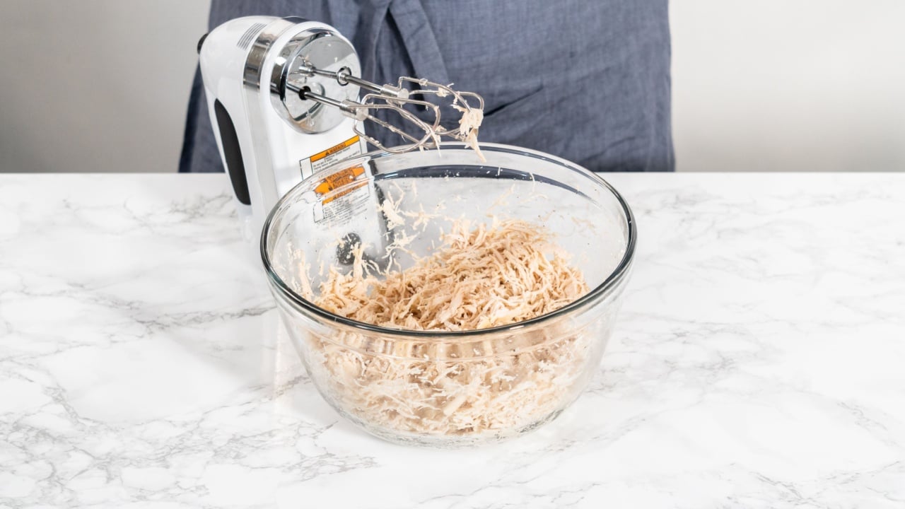 Shredded chicken in a pressure cooker. Shredding freshly cooked chicken breast in a glass mixing bowl with a hand mixer.