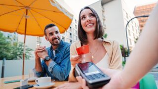 Happy couple paying the bill of the coffee shop using a contactless creditcard payment. Young adult customer woman doing a purchase on a restaurant to the cashier with a debit card. People spending