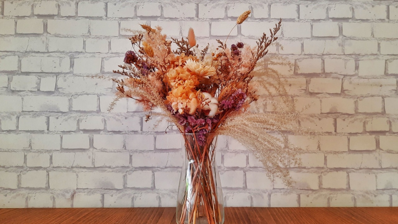 Bouquet of dried flowers and leaves in a transparent glass vase. Beautiful room decoration. Bouquet of flower vase on table with white brick background. Place for writing text.
