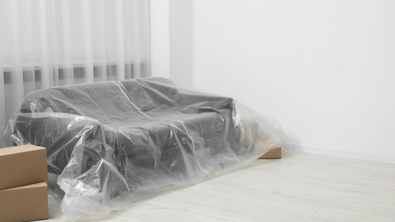 Stylish sofa covered with plastic film and boxes at home. Space for text