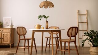 The stylish dining room with round table, rattan chair, wooden commode, pock up poster and kitchen accessories. Beige wall with mock up poster. Home decor. Template.