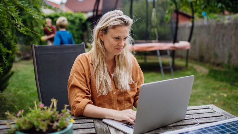 Businesswoman, freelancer or manager working outdoors in garden, garden homeoffice. Remote work from backyard. Laptop is charging with solar charger. Concept of working remotely.