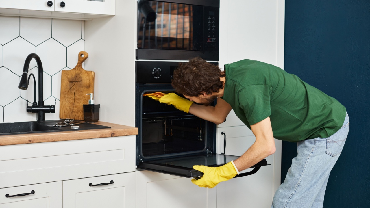 good looking man in casual dark green t shirt washing attentively his oven during spring cleaning