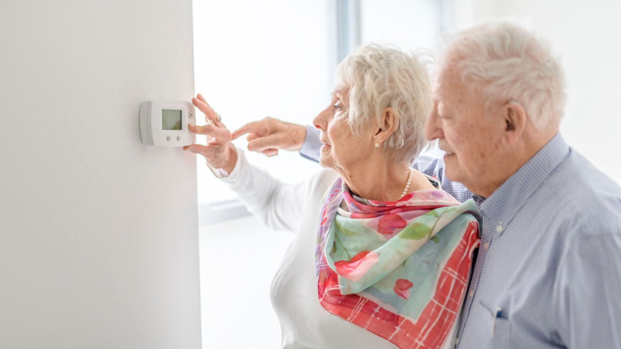 A senior lady posing at home portrait close to a window using thermostat