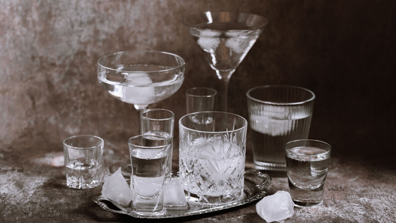 Collection of various glasses on silver tray filled with clear cold drinks with ice on grunge wall background