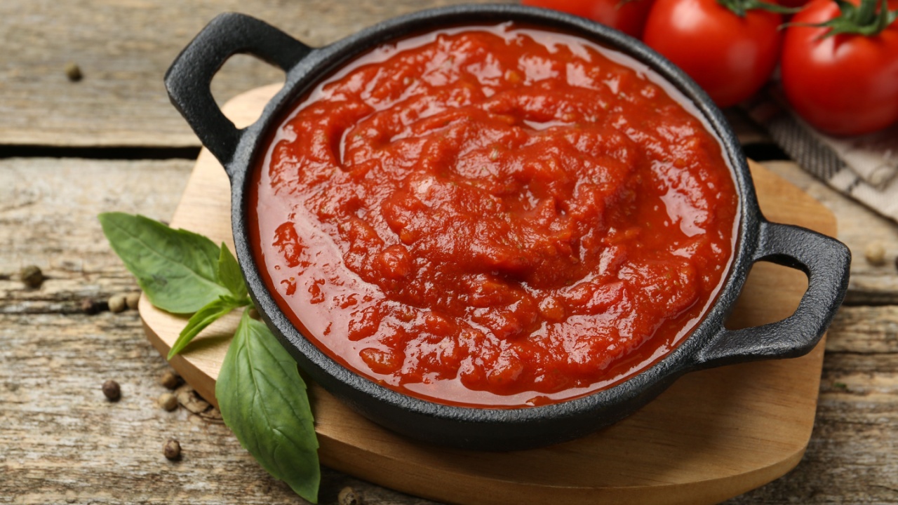 Homemade tomato sauce in bowl and basil on wooden table, closeup