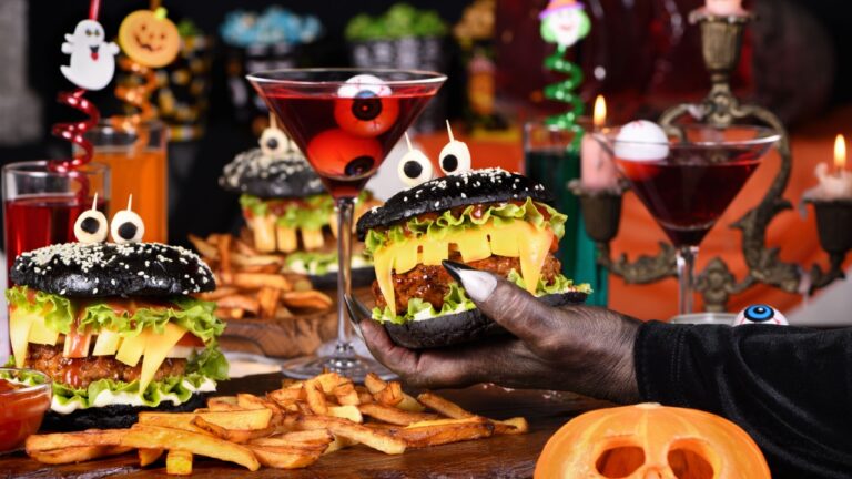 A witch's hand takes a Witch cocktail with eyeballs in a martini glass from the Halloween party table.