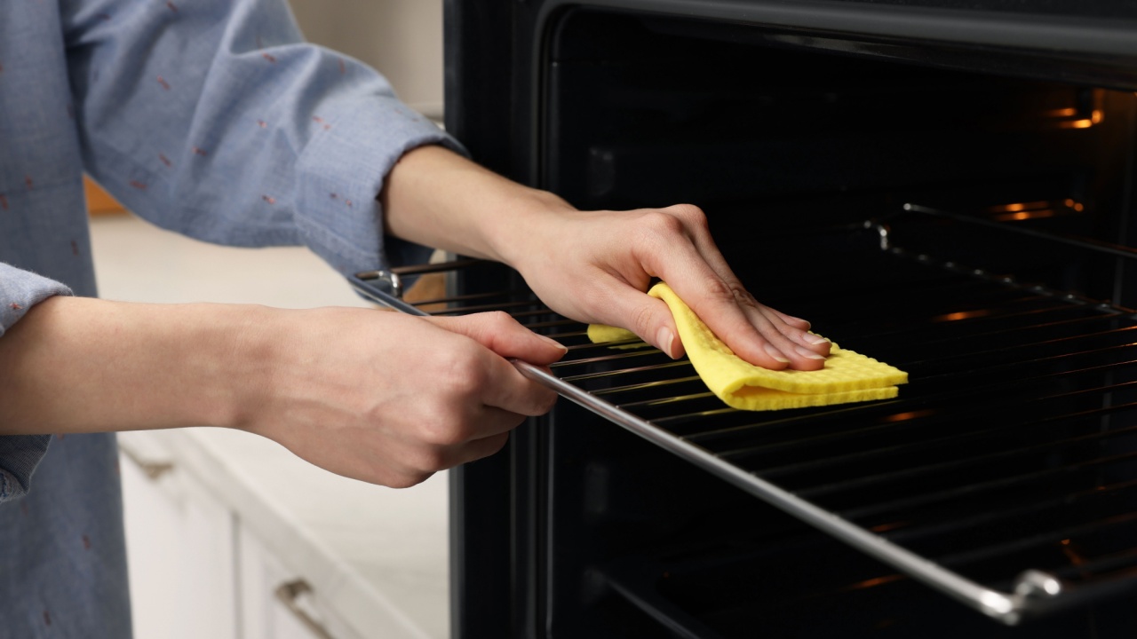 Woman cleaning oven rack with rag in kitchen, closeup
