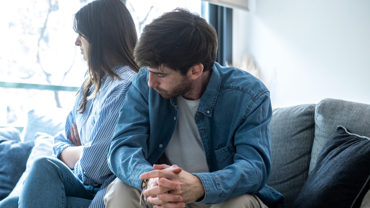 Young adult couple at home after discussion upset with man asking sorry to woman sitting and ignoring him looking outside the window. Relationship break up divorce concept moment. Tension financial