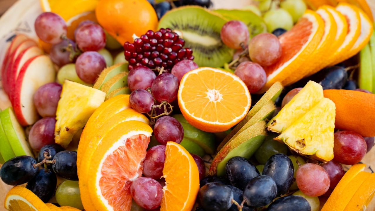 On the surface of a wooden cutting board, there is an appealing assortment of different types of fruit arranged beautifully, showcasing vibrant colors and varied textures that invite enjoyment