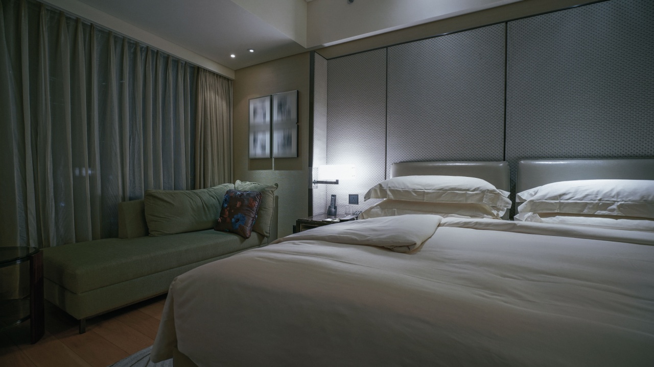 A cozy and luxurious bedroom featuring a large bed with plush white bedding and a padded headboard. The room is dimly lit, creating a relaxing ambiance.