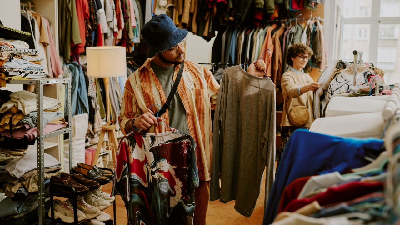 Person browsing racks of clothing in bright thrift store with various garments on display during daylight Peering at different shirts and examining styles and options