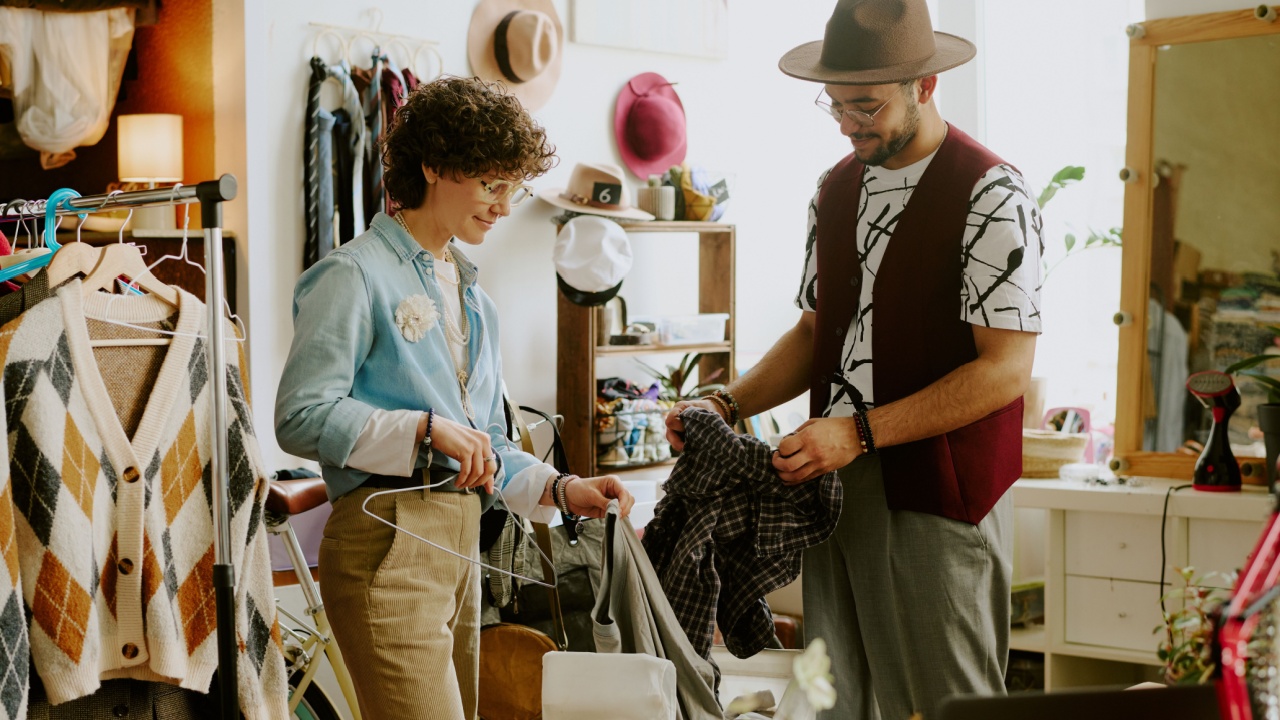 Two people engaged in sorting clothes in a vintage clothing store surrounded by various clothing items and accessories creating a well-organized setting