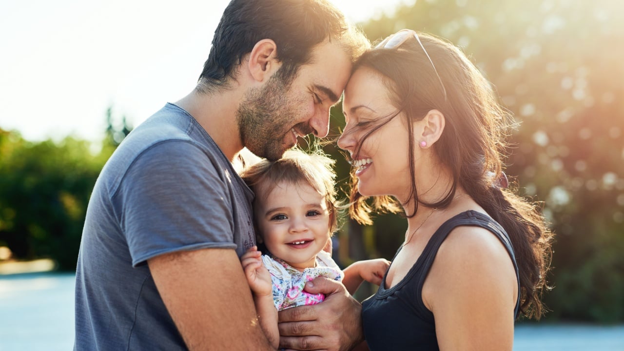 Happy, love and parents with baby in park for bonding, loving relationship and relax together outdoors. Family, sunshine and mom, dad and child for embrace, affection and forehead touch on weekend