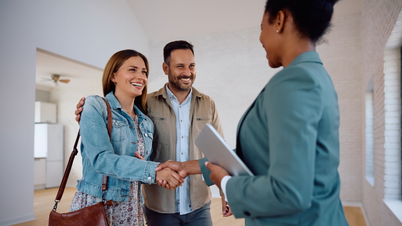 Happy woman shaking hands with real estate agent while buying new apartment with her husband.