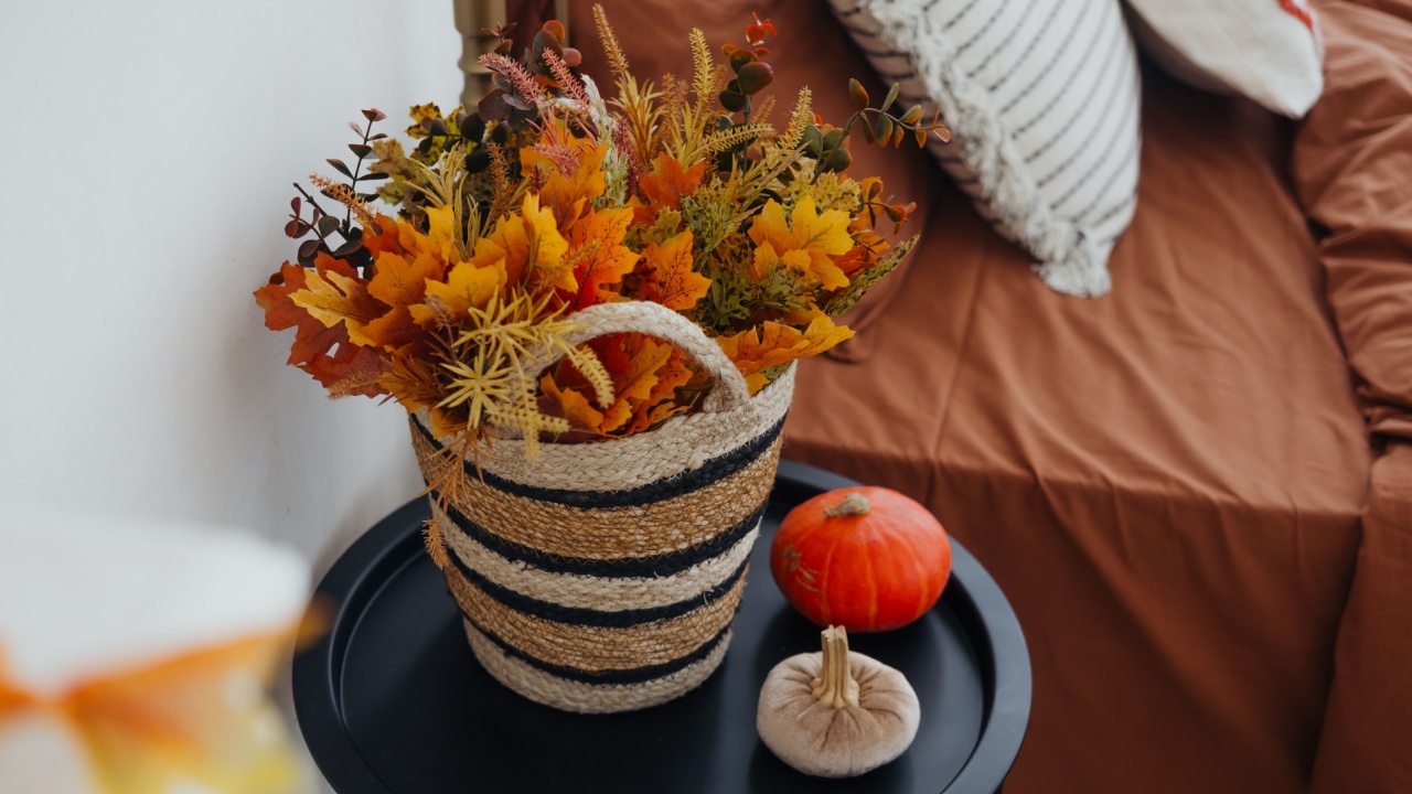 A woven basket filled with autumn foliage sits next to a small pumpkin on a black table.