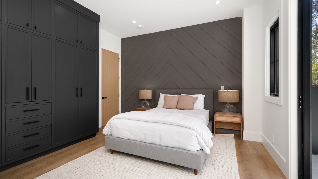 Modern bedroom with dark built-in wardrobes, a cozy bed, and wooden side tables, featuring a chevron-patterned accent wall and natural light.