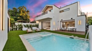 Modern luxury home with pool and outdoor seating at sunset, showcasing elegant architecture and vibrant sky.