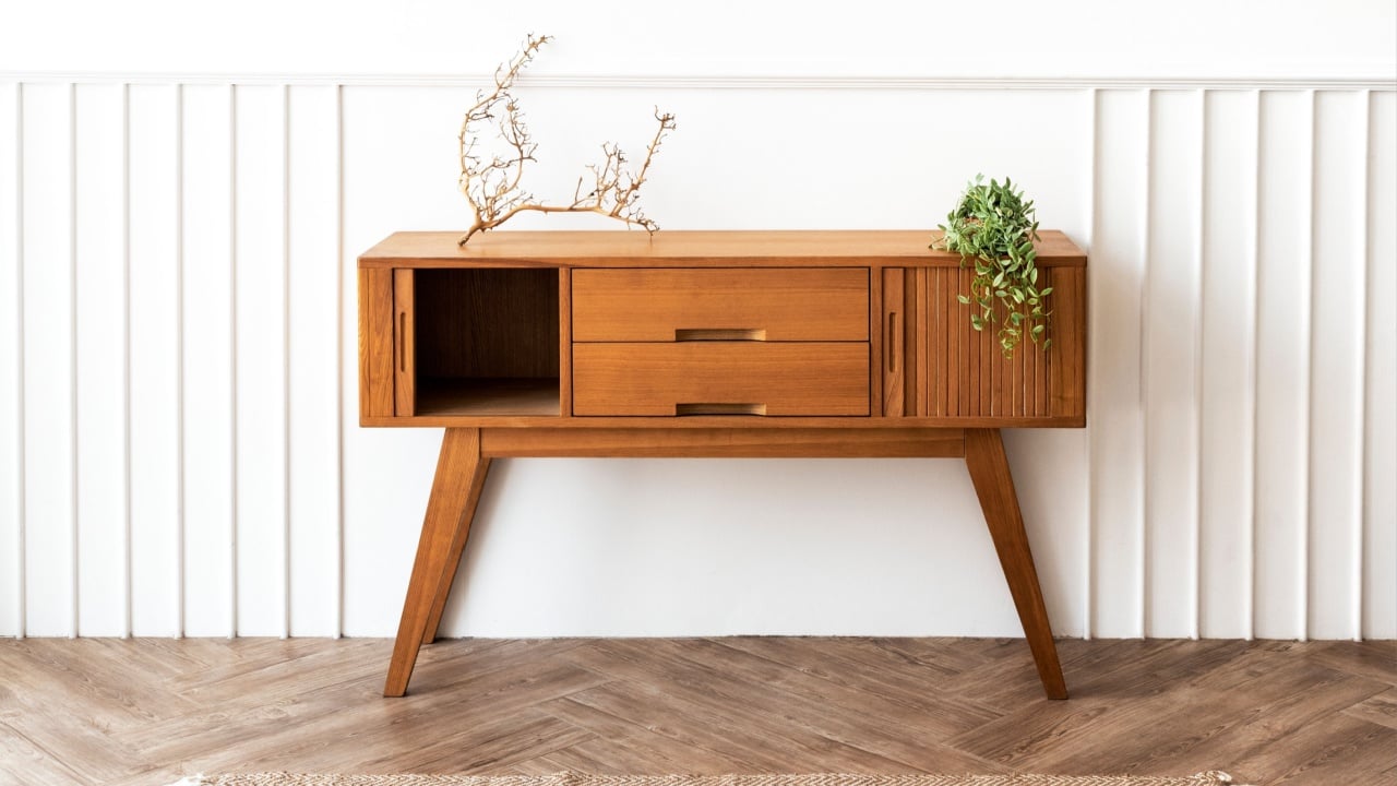 Mid-century modern wooden sideboard with drawers and open shelf. Elegant wooden design, perfect for storage. Wooden sideboard with decorative plants against white wall and herringbone wooden floor.