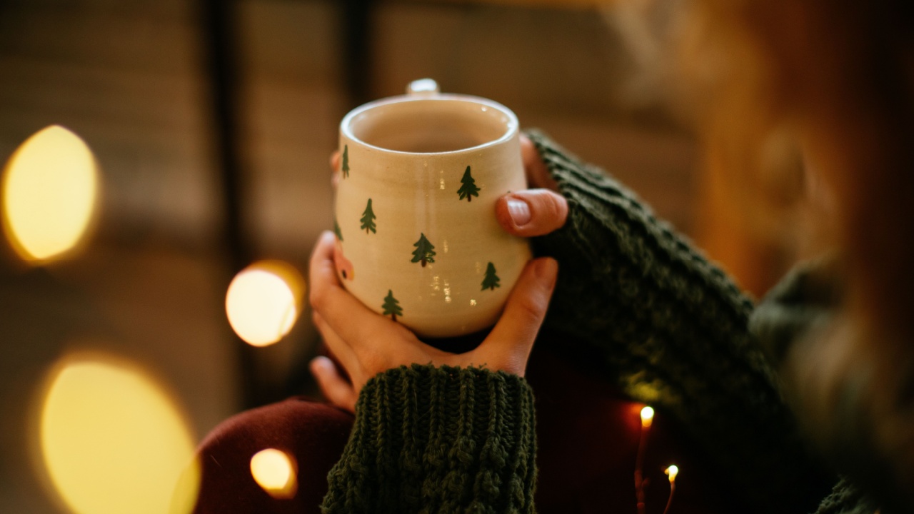 Christmas mug held in woman hands, capturing the cozy holiday spirit. Close-up of woman hands gently holding a Christmas and New Year themed mug, creating a warm and cozy holiday atmosphere