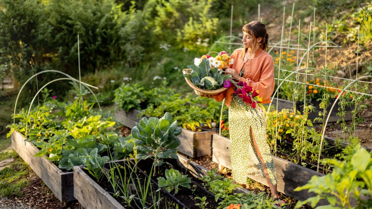 A young woman holding a basket filled with freshly harvested vegetables and vibrant flowers in a sunlit garden. A moment capturing the essence of sustainable living and natural beauty