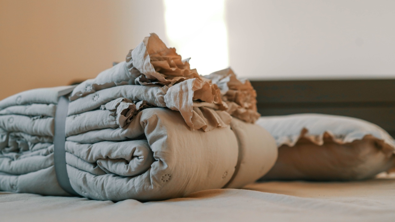 Cozy beige bedding set with ruffled details, neatly folded and placed on a bed in a warmly lit bedroom. Highlights themes of comfort, elegance, and minimalistic home decor.