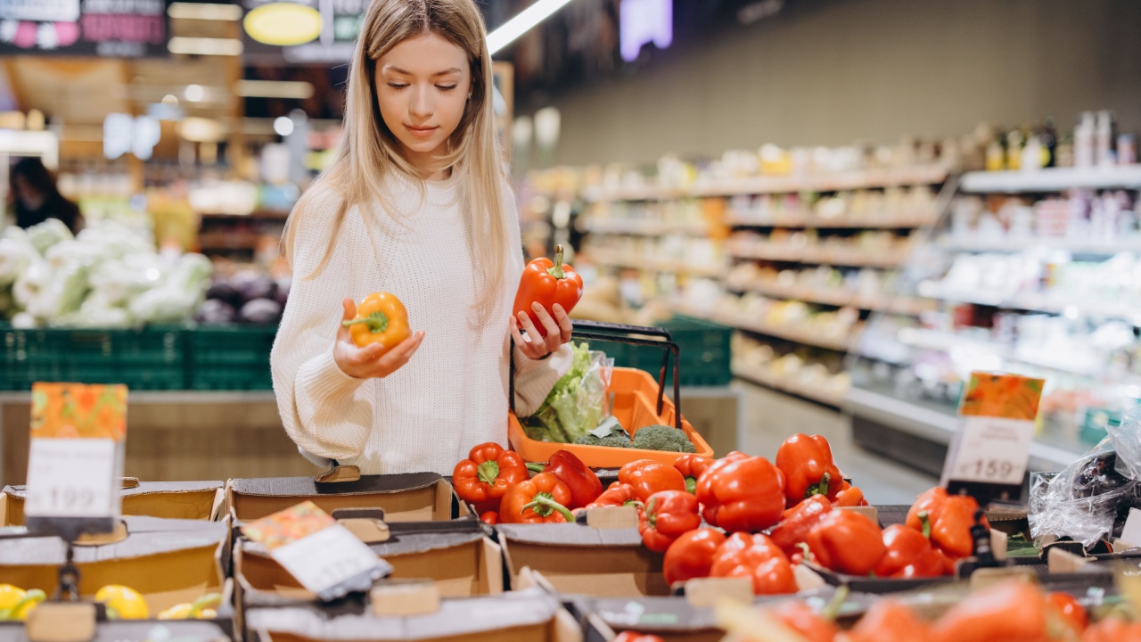 Customer comparing yellow and red bell peppers while shopping for groceries in a supermarket