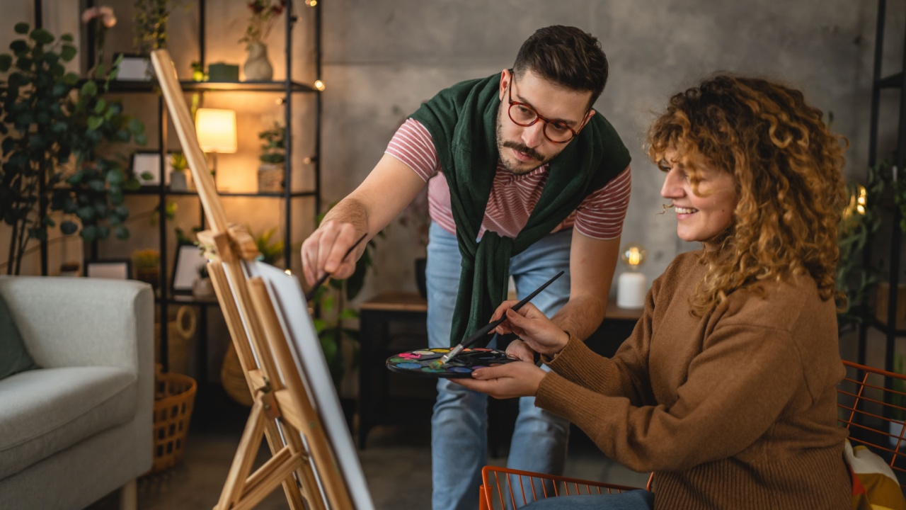 Adult couple paint on canvas easel, girlfriend learn from boyfriend how to do painting and hold brush at home