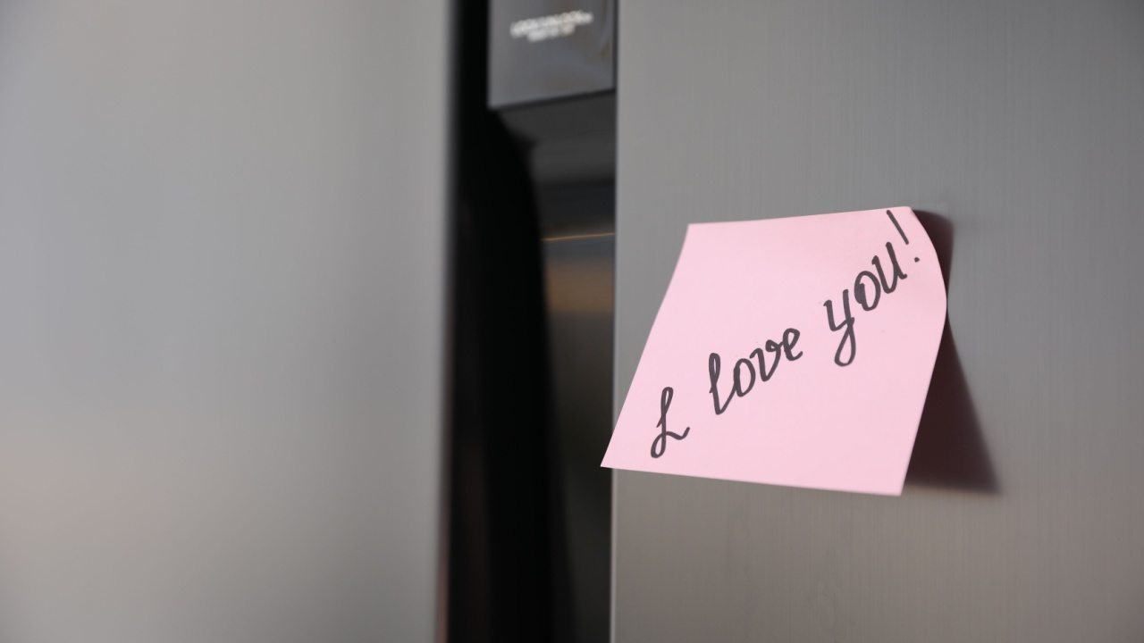 Sticky note with handwritten text I Love You attached to fridge door. Romantic message