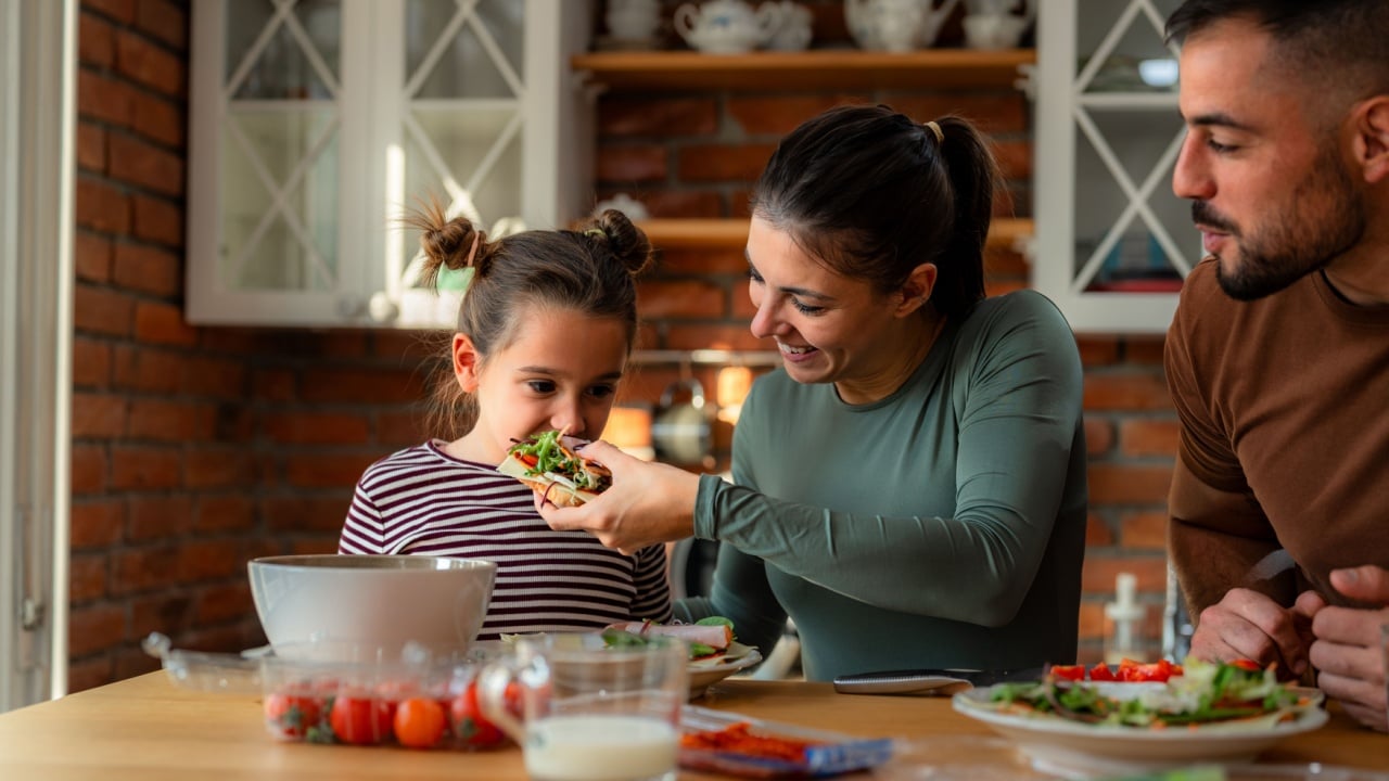 Family members take turns offering healthy bites to one another as they make breakfast in their home.