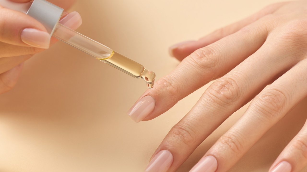 A hand is shown delicately applying a nourishing oil with a dropper to another hand's nails. This self-care moment emphasizes the importance of nail health and grooming.