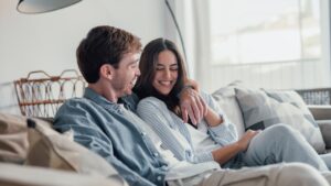 Portrait of young 20s just married couple in love posing photo shooting seated on couch in modern studio apartments, concept of capture happy moment, harmonic relationships, care and sincere feelings