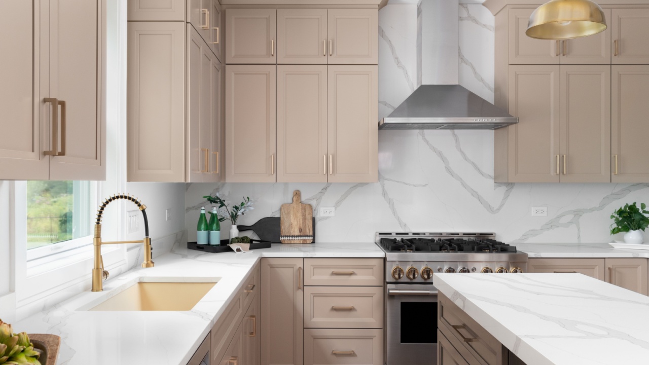 Naperville, IL, USA - August 2, 2023: A kitchen detail with brown cabinets, marble countertop and backsplash, wood island, and gold faucet, sink, and light fixtures. No brands or labels.