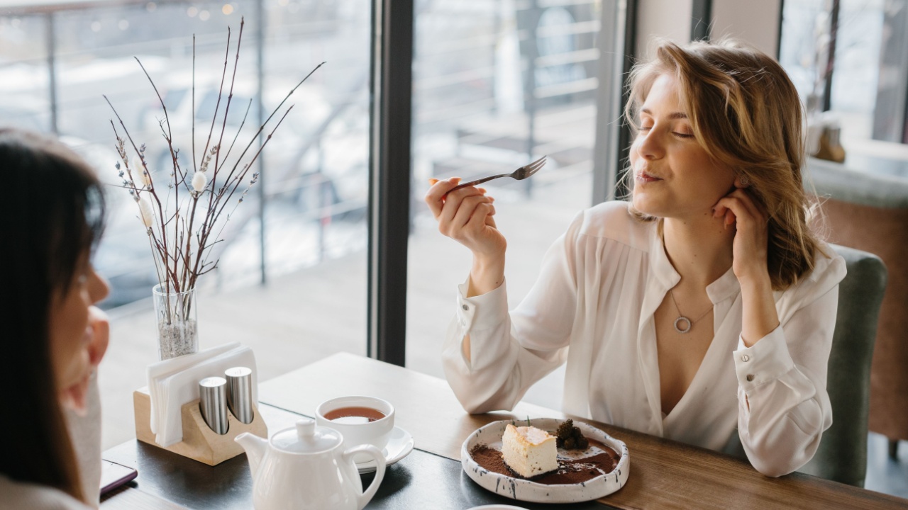 A content woman savoring dessert and tea in a cozy cafe, showcasing relaxation and indulgence in a serene setting. The moment encapsulates joy and the art of enjoying simple pleasures.
