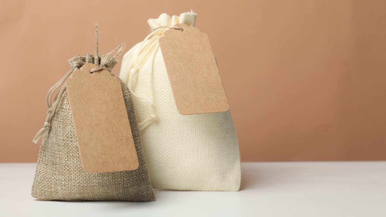 Burlap bags with tags on white marble table against dark beige background, space for text