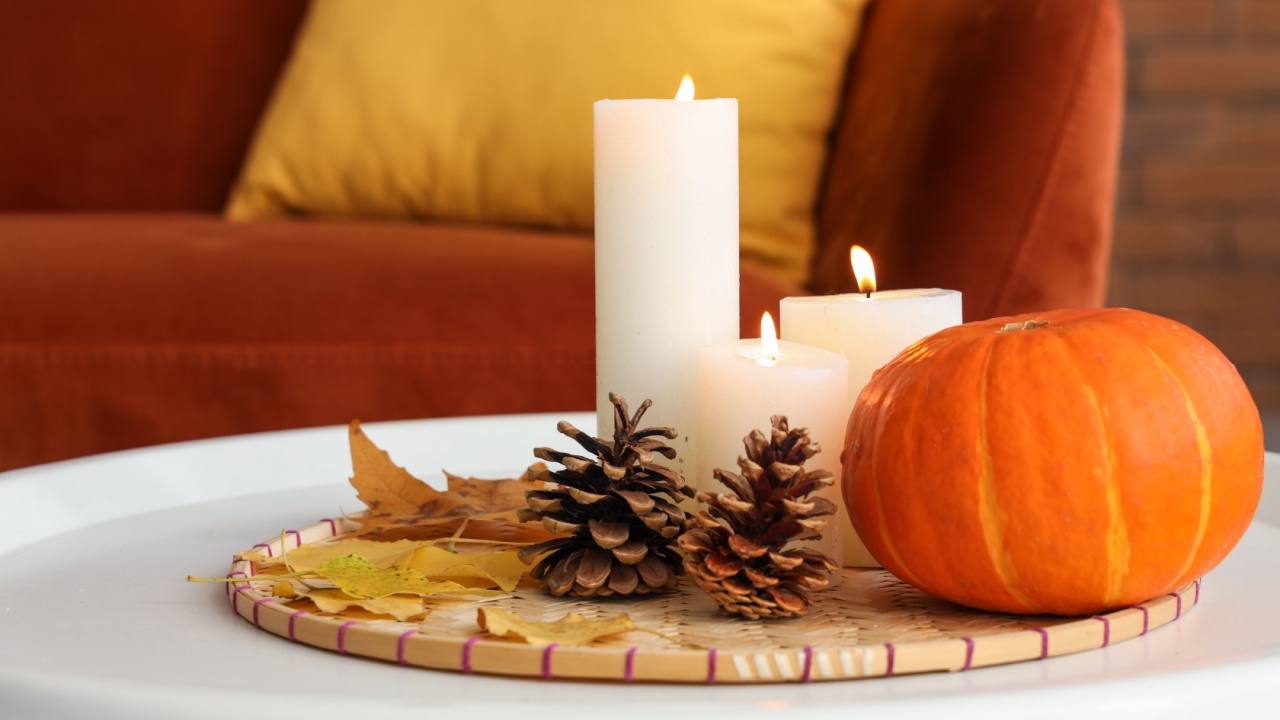 Burning candles, pumpkin, cones and autumn leaves on coffee table in living room. Closeup