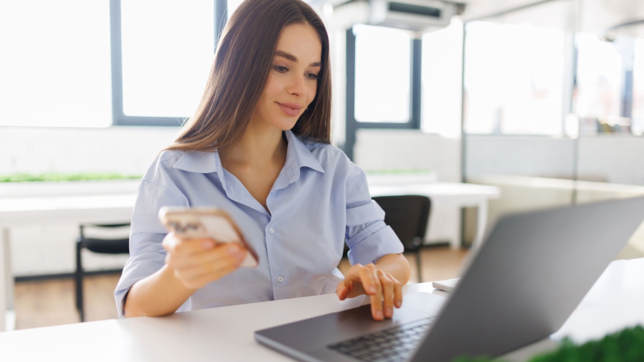 Young happy business woman, smiling beautiful professional lady worker looking at smartphone using cellphone mobile cellular tech working at home or in office checking cell phone sitting at desk.
