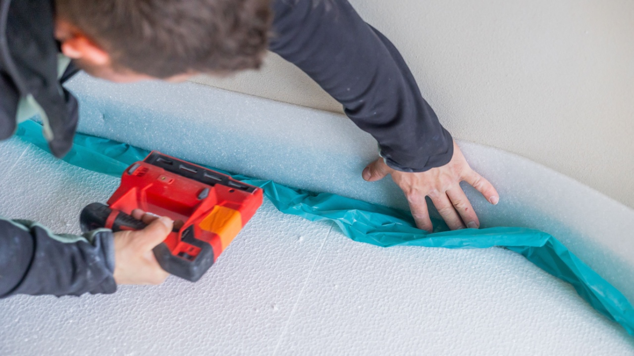 Construction worker installing vapor barrier on insulated wall with staple gun